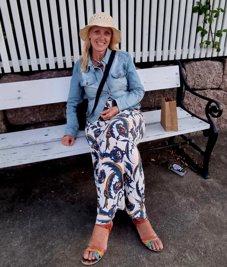 Merete sitter på en benk en varm sommerdag