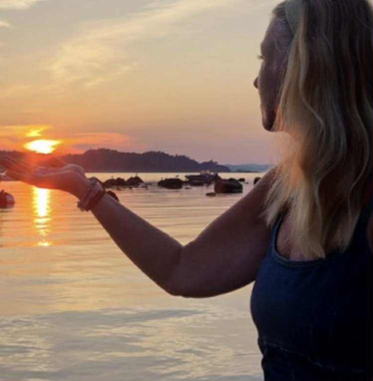Merete holder solen i hånden ved havet i solnedgang